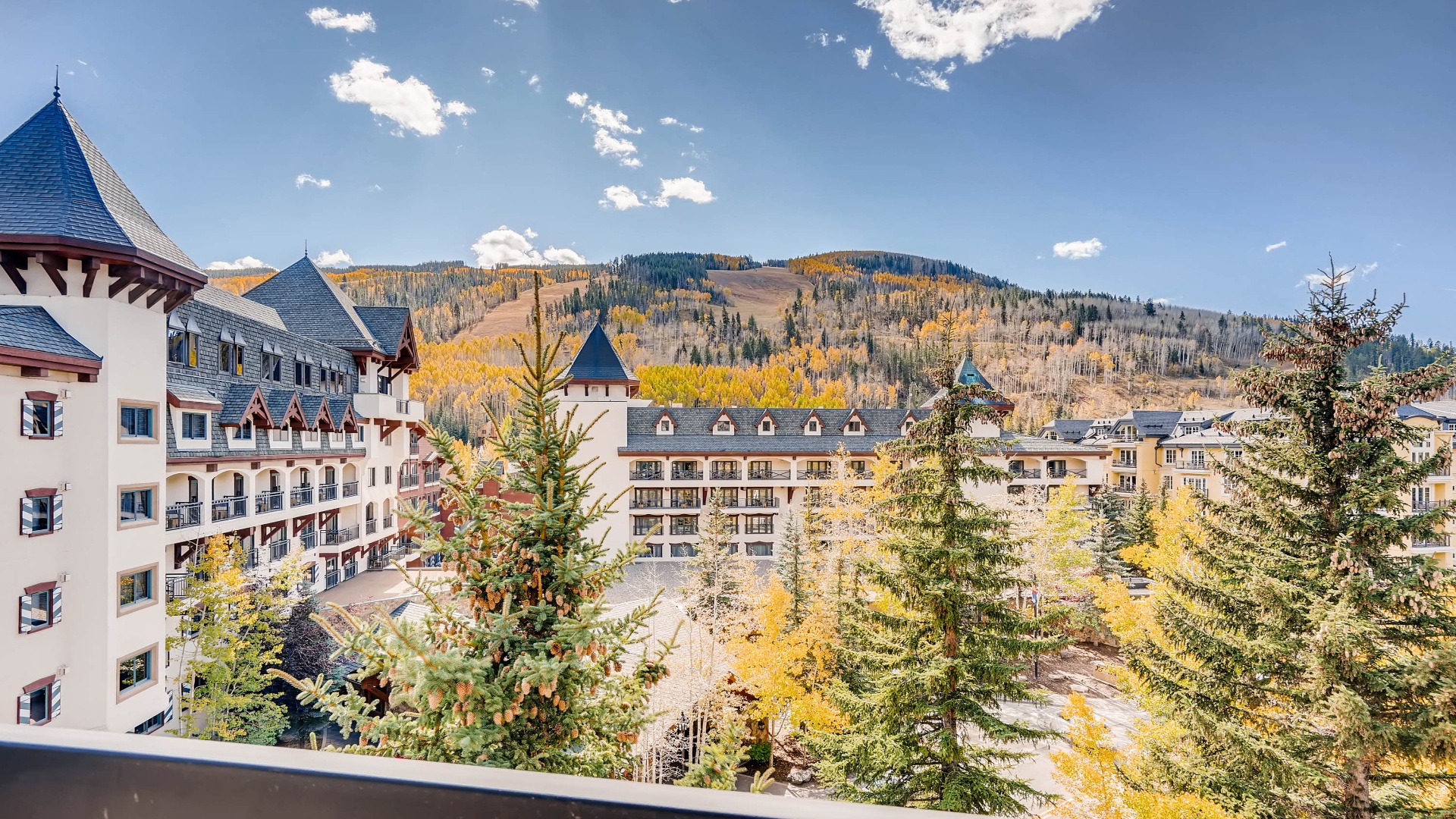 Alpine village nestled below stunning mountain peaks surrounded by golden autumn aspens and evergreen forests during fall season.