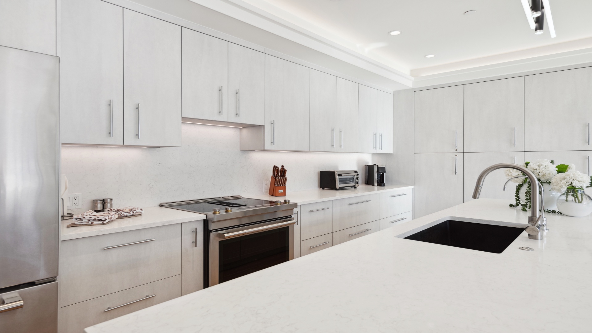 A pristine, modern kitchen awaits you with sleek white cabinetry, stone countertops, stainless appliances, and ample prep space for cooking your favorite meals in style.