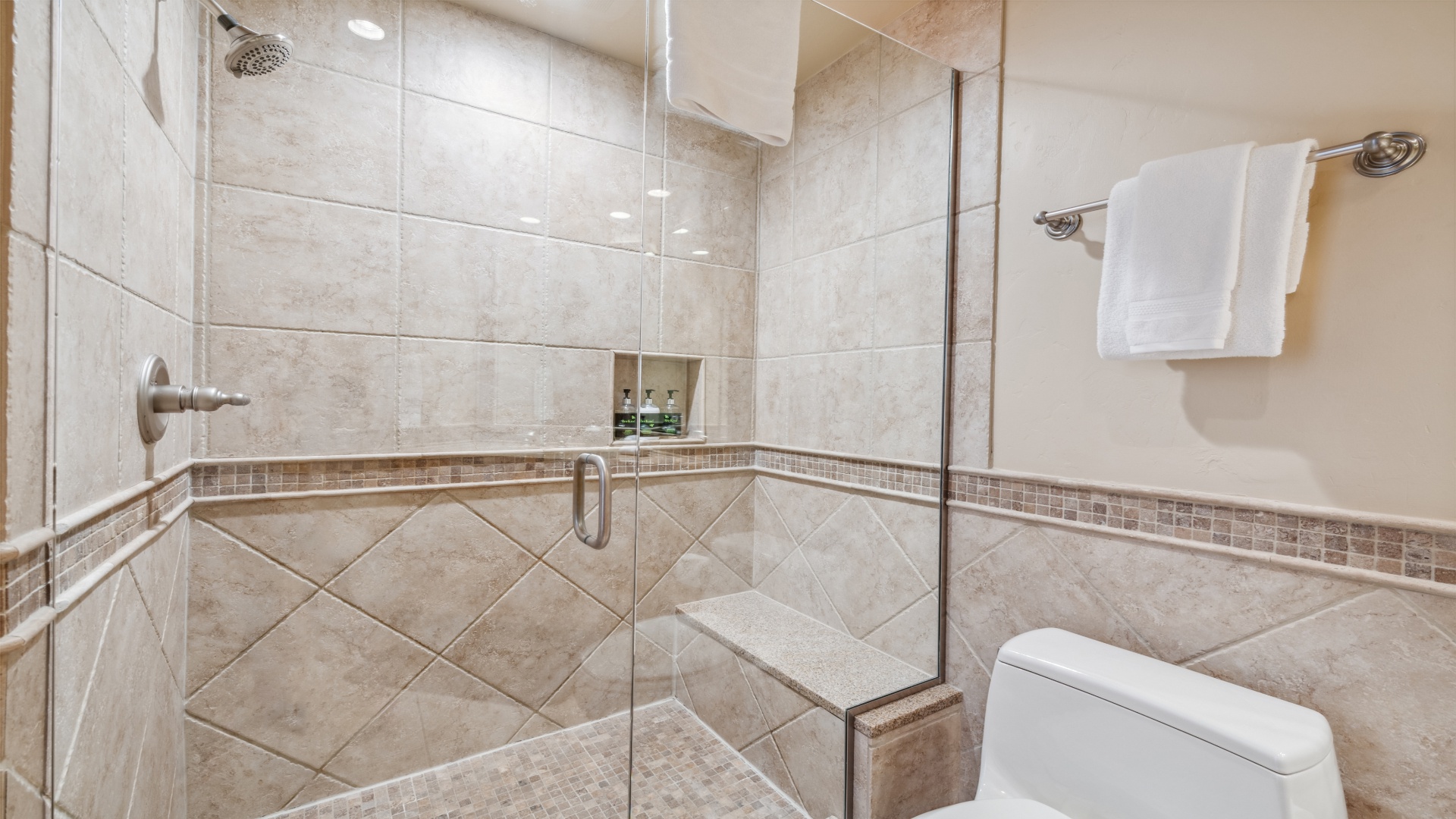 Slip into your private spa-like sanctuary featuring a spacious walk-in shower with elegant tilework, a rainfall showerhead, built-in niche for toiletries, and plush white towels waiting to wrap you in comfort.