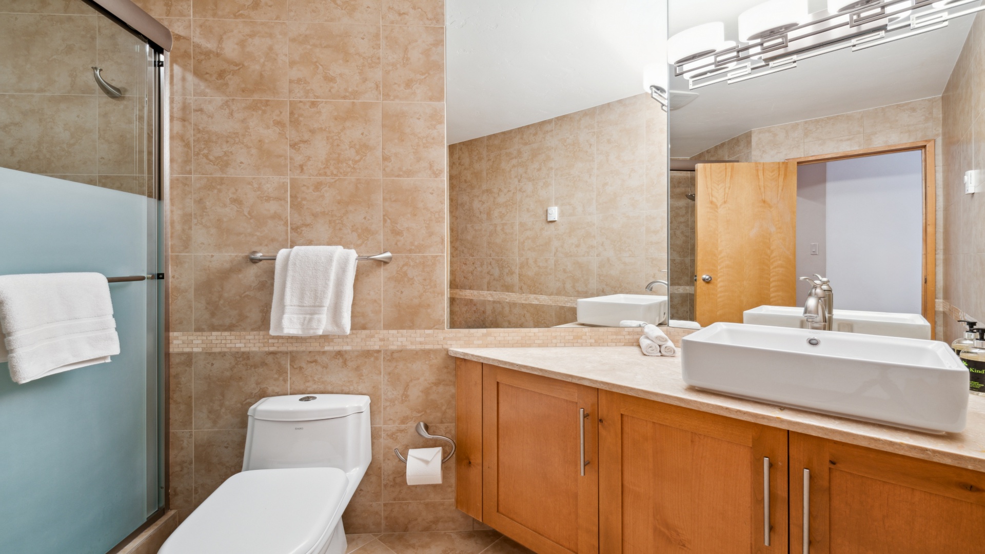 Step into your private spa-like bathroom, featuring warm travertine tiles, a spacious walk-in shower, and elegant vessel sink—all yours to enjoy after a day of exploring.
