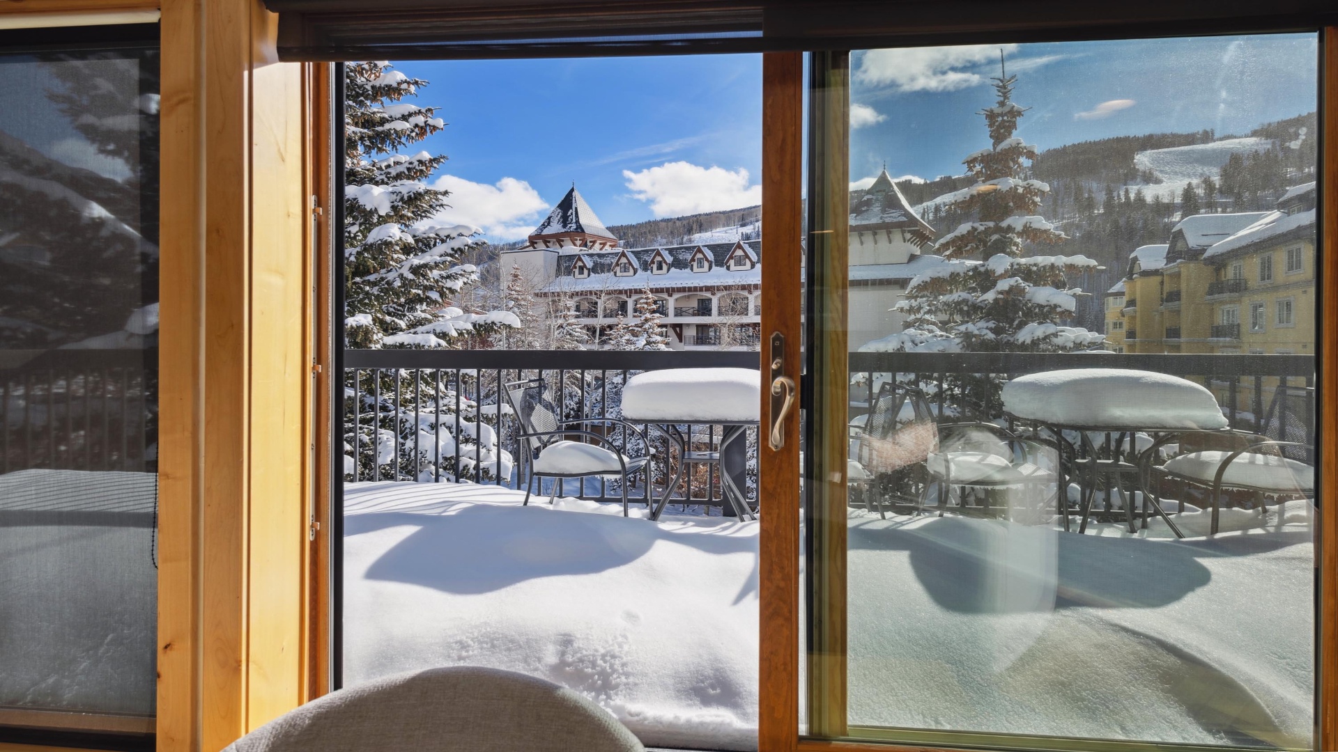 Step through open doors to a snow-blanketed balcony. Fresh powder, evergreens, and a charming alpine village provide a serene mountain escape right outside your room.
