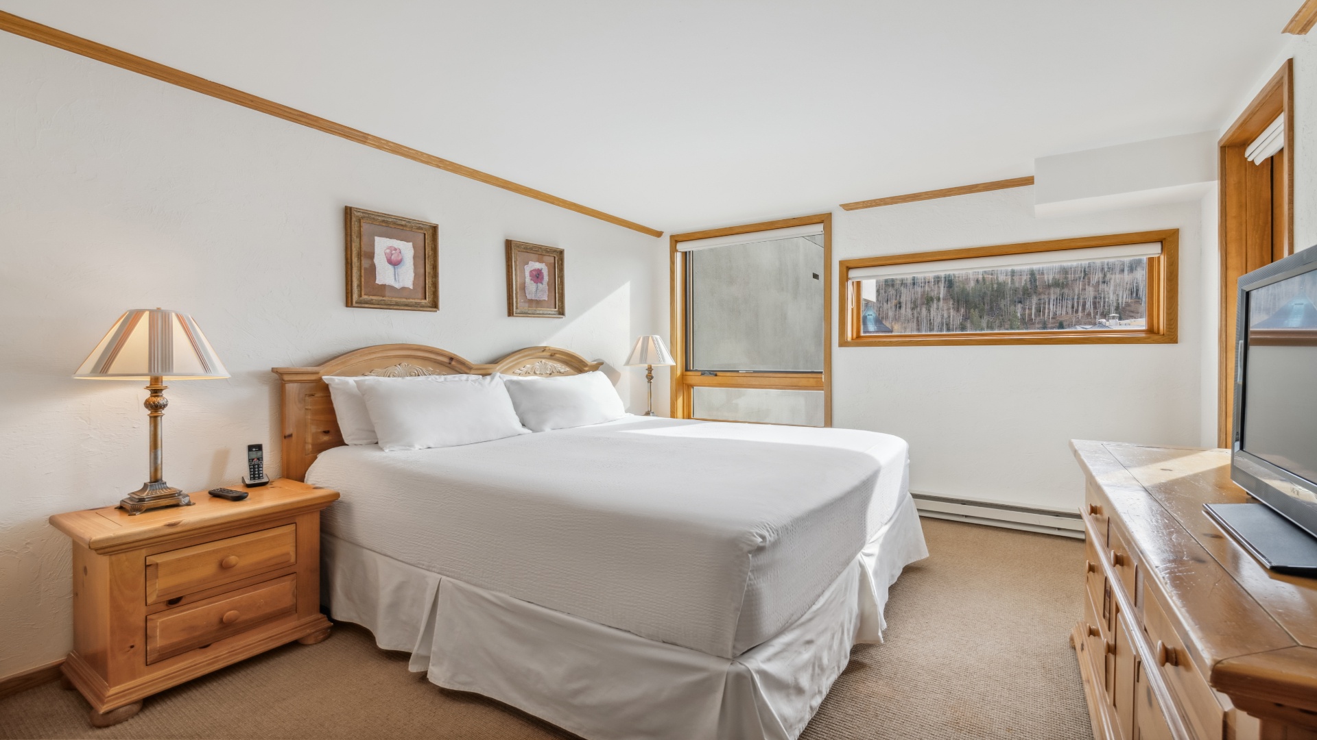 Your spacious bedroom features a plush king bed with crisp linens, warm wood furnishings, soft bedside lighting, and a convenient TV—perfect for unwinding after a day of adventure.