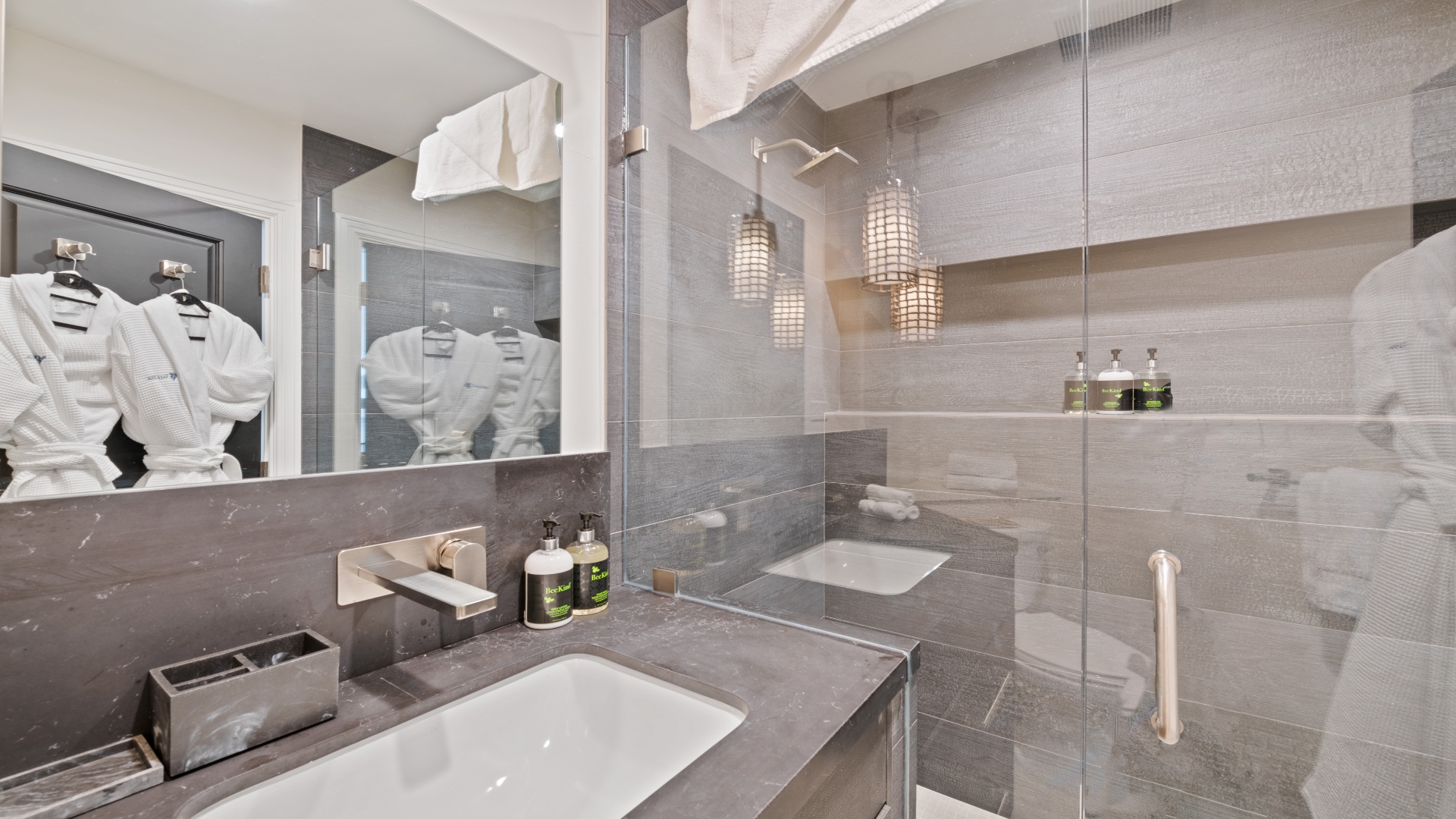 Step into your modern spa-like bathroom, where sleek gray tones, elegant pendant lighting, and plush robes await to make your stay feel effortlessly luxurious.