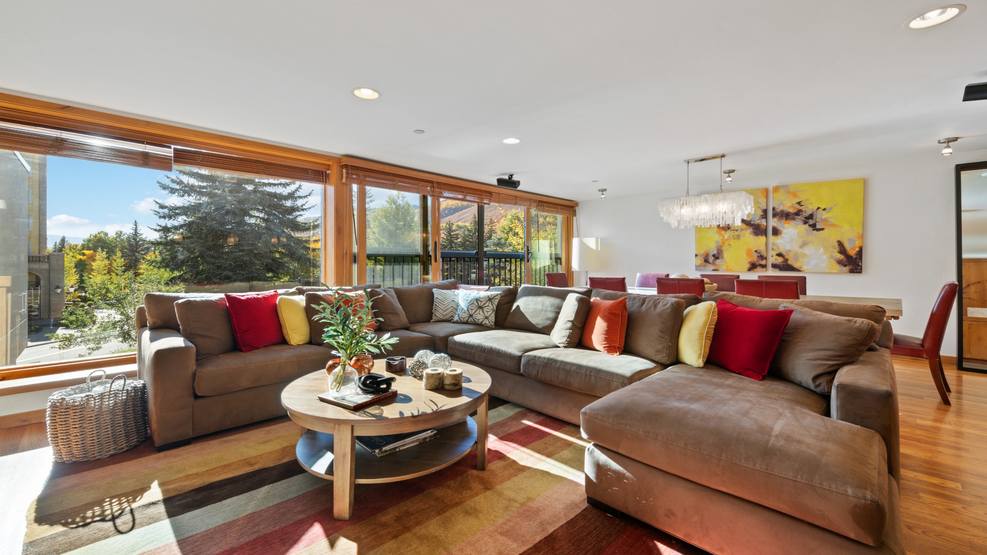 Sink into plush sectional seating bathed in natural light from floor-to-ceiling windows showcasing vibrant autumn foliage. Your open-plan living and dining area offers warmth, color, and serene views.