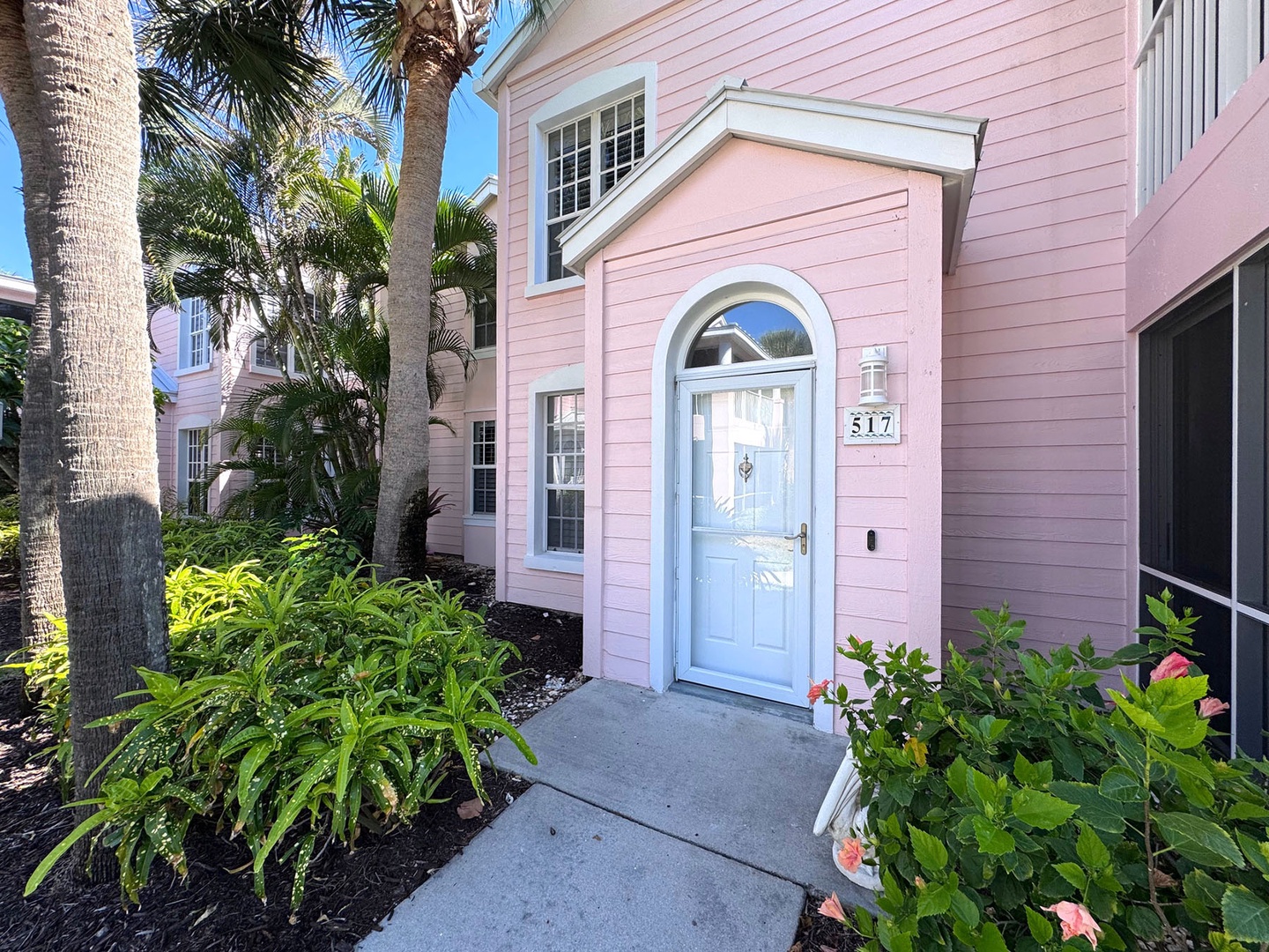 Charming pink cottage with tropical landscaping and palm trees creates a welcoming arrival at this coastal retreat.