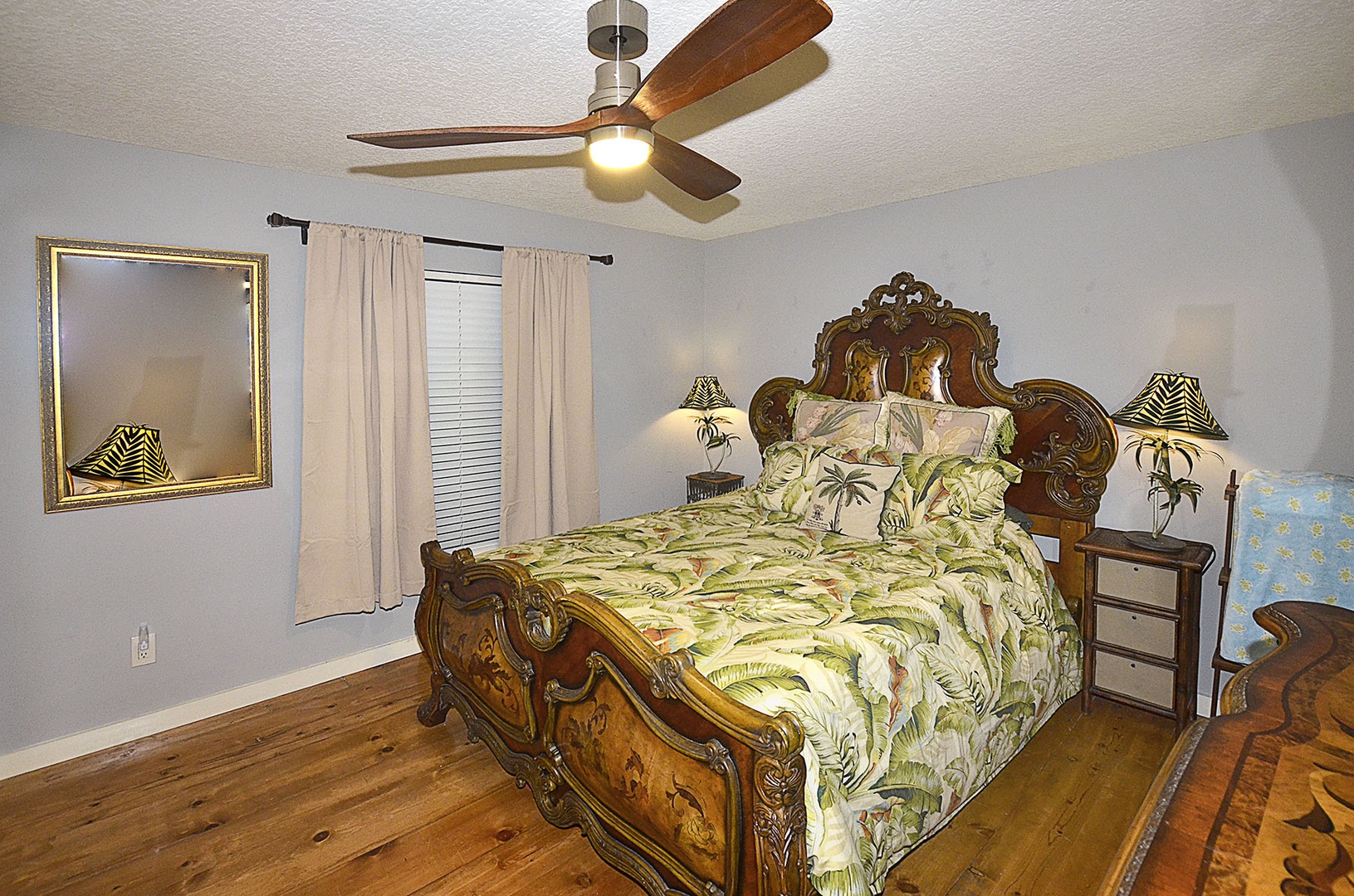 Guest Bedroom. Drift off in this elegant bedroom featuring a stunning carved wood bed, tropical-themed linens, and gentle ceiling fan for perfect comfort.