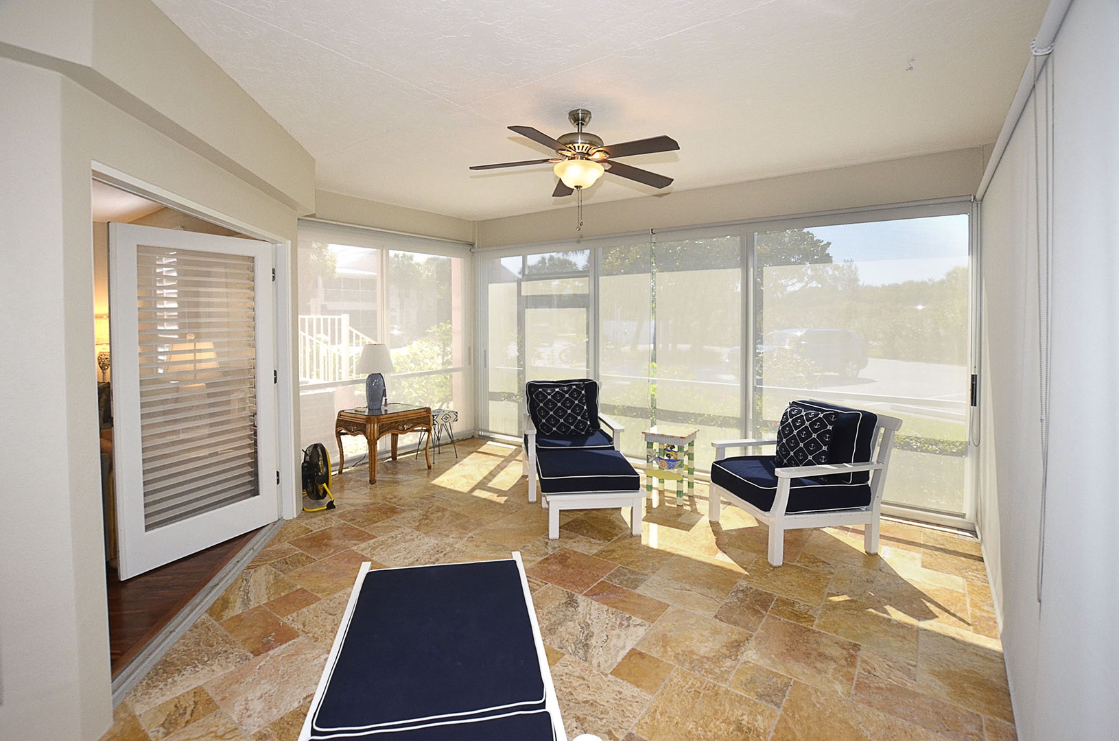 Unwind in your bright sunroom with navy seating and natural stone floors, where afternoon light filters through floor-to-ceiling windows.