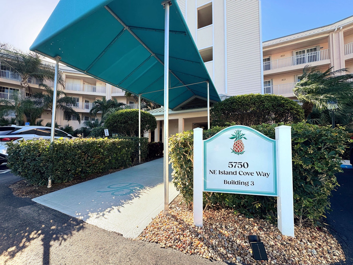 Property entrance at 5750 NE Island Cove Way Building 3, featuring tropical landscaping and multi-story residential buildings.