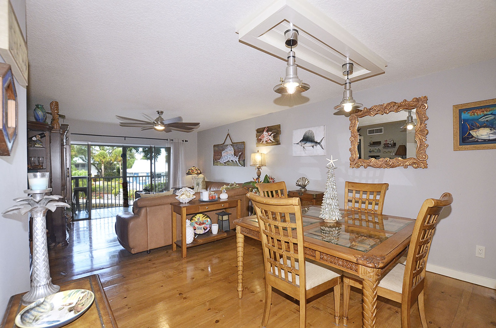Dining / Living / Balcony. Open dining and living space features warm wood flooring and coastal-themed decor for relaxing comfort.