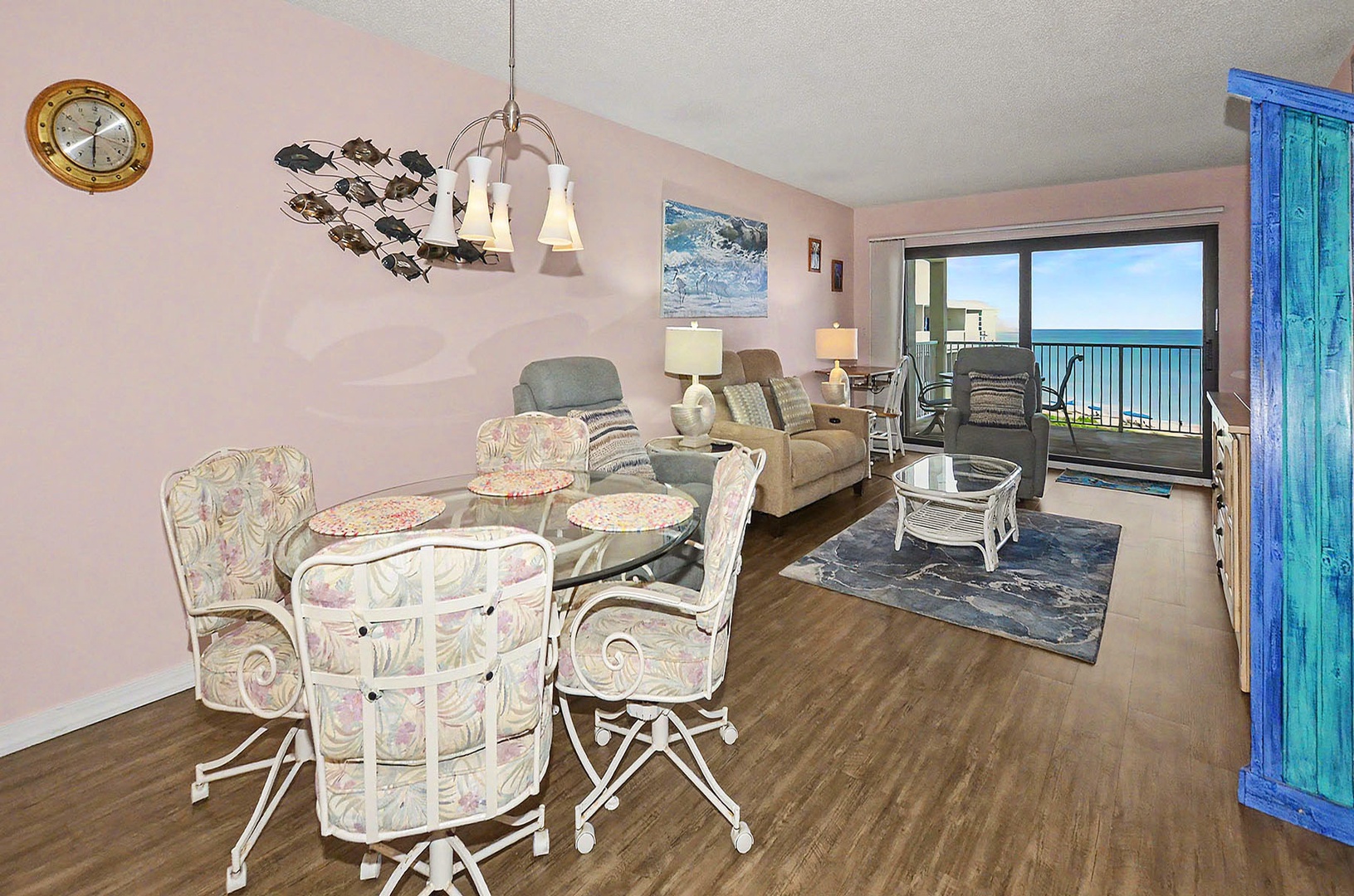 Dining / Living / Balcony. Open dining and living space features warm wood flooring and coastal-themed decor for relaxing comfort.