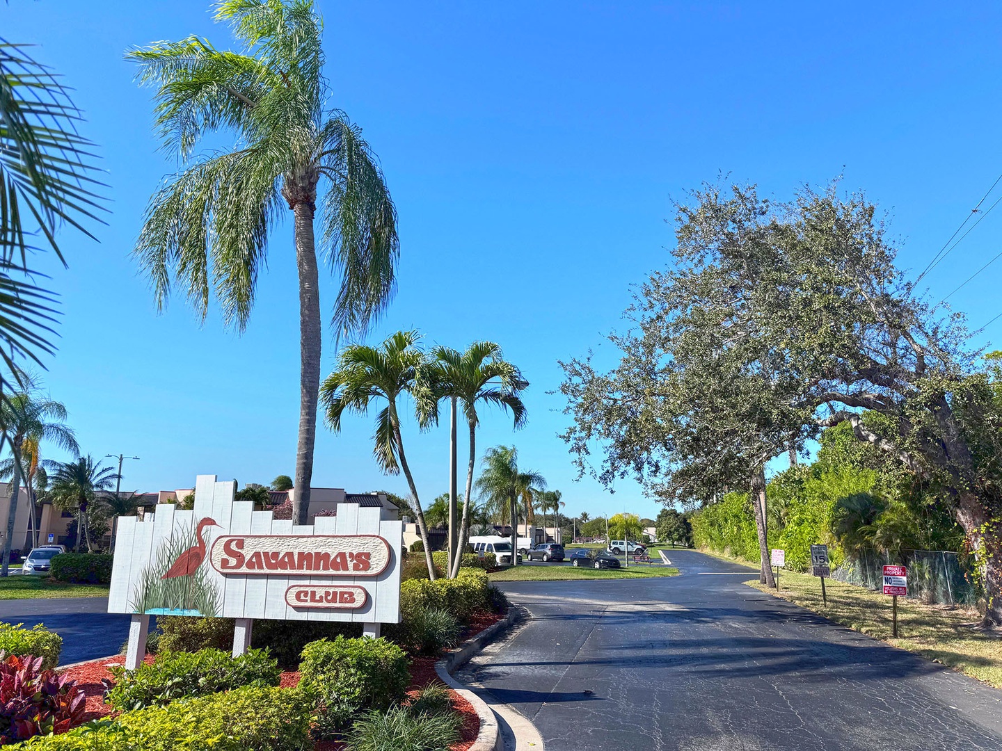 Palm-lined entrance to Savanna's Club community features tropical landscaping and clear blue skies welcoming arrivals.