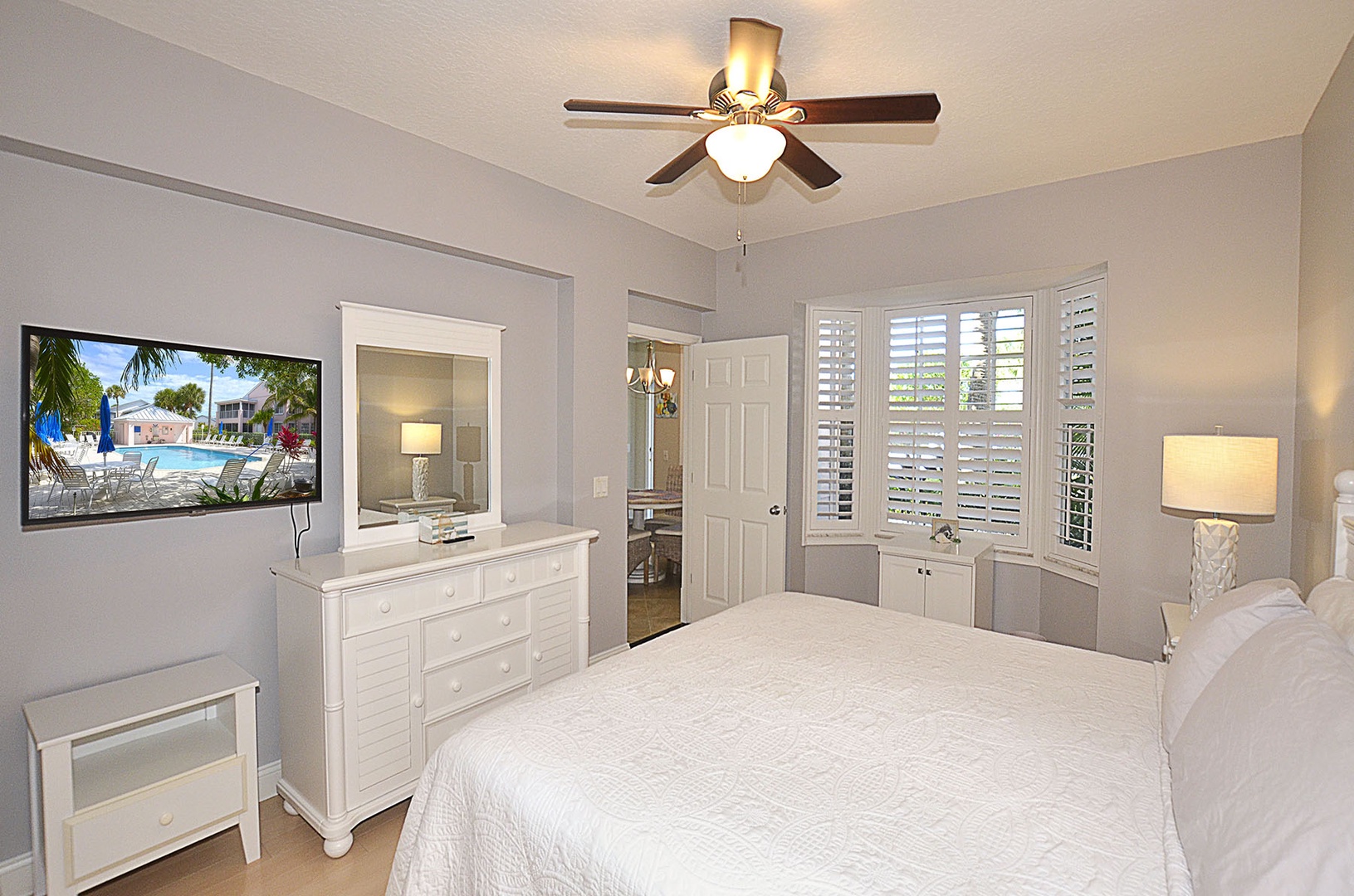 Peaceful Main bedroom sanctuary, complete with ceiling fan,  wall-mounted TV, and plantation shutters filtering gentle sunlight.