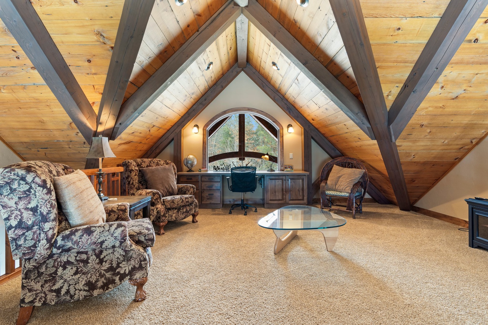 Escape to your private attic retreat with soaring timber beams, cozy seating, and a charming arched window overlooking nature.