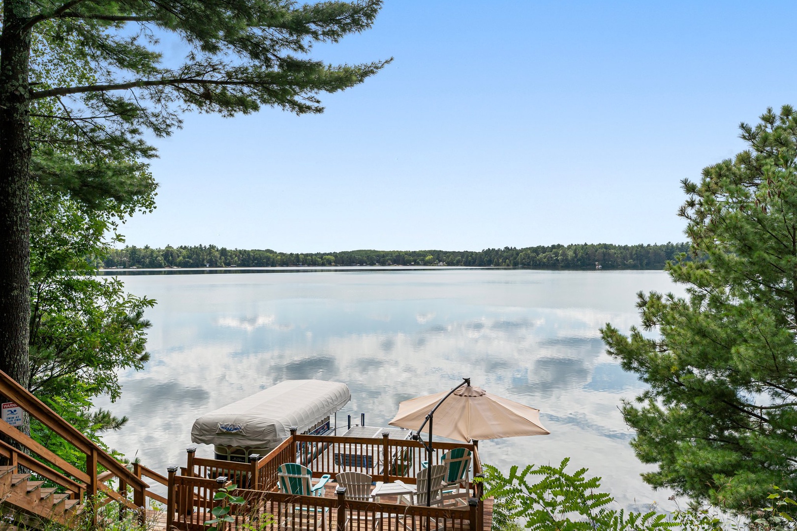 Peaceful lakefront deck with seating and umbrella overlooking pristine waters surrounded by lush forest.
