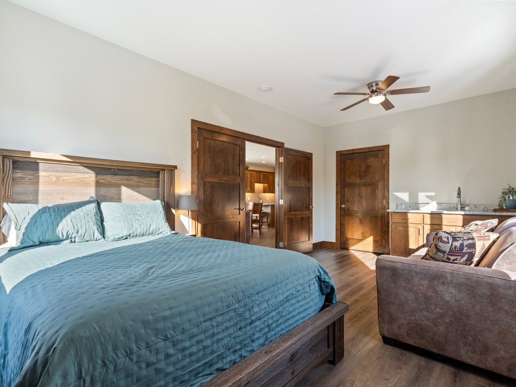 Unwind in your spacious bedroom featuring rich wood accents, plush turquoise bedding, and a cozy reading chair beneath the gentle ceiling fan.