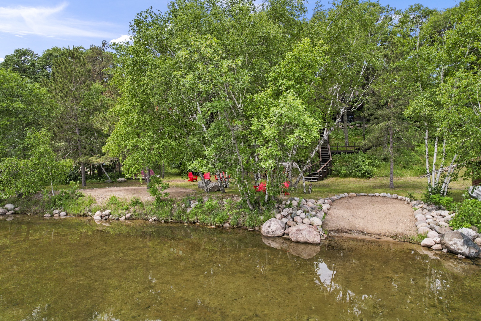 Expansive lakefront setting with natural stone shoreline, mature trees, and outdoor seating areas creating a peaceful retreat atmosphere.