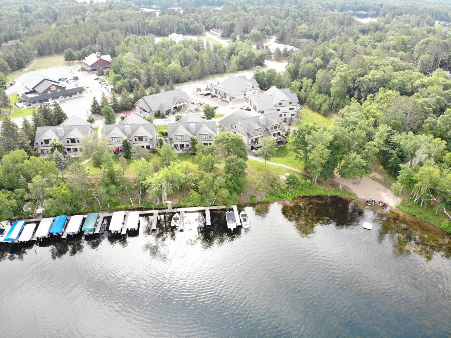 Aerial view of lakefront property featuring multiple buildings, private dock with boat slips, and forested surroundings in a peaceful setting.