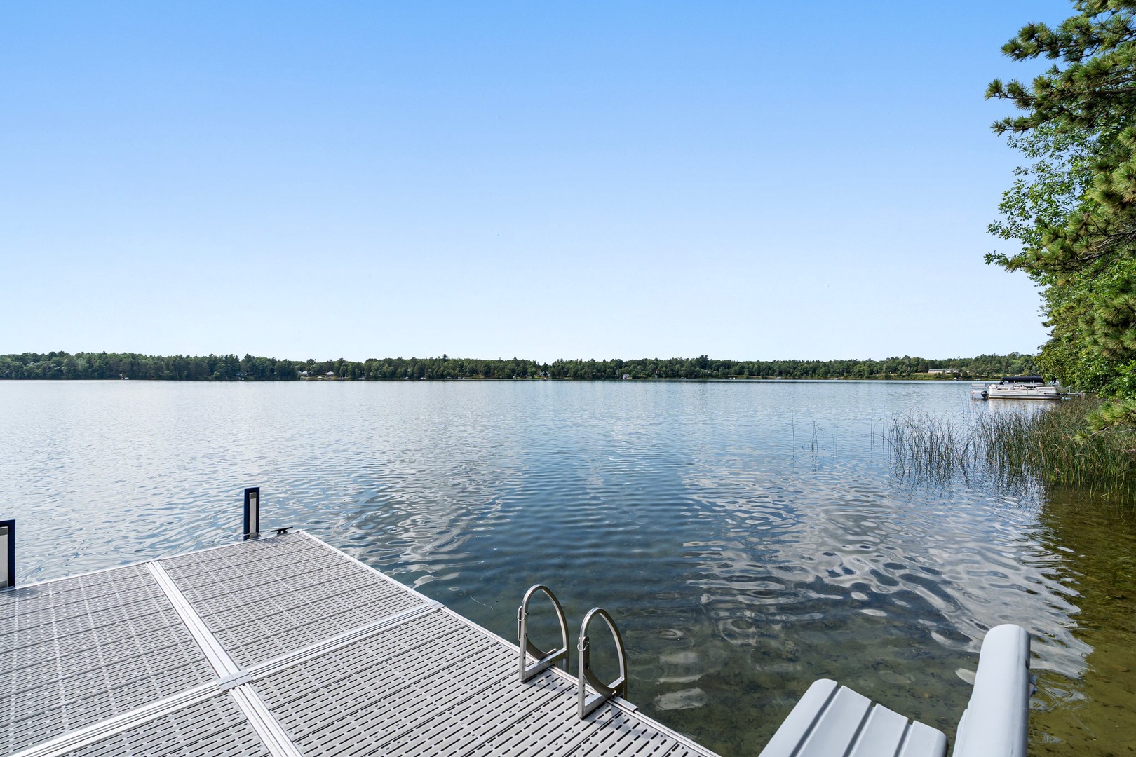 Pristine lake stretches before the property's private dock, offering tranquil waters for swimming and peaceful moments by the shore.