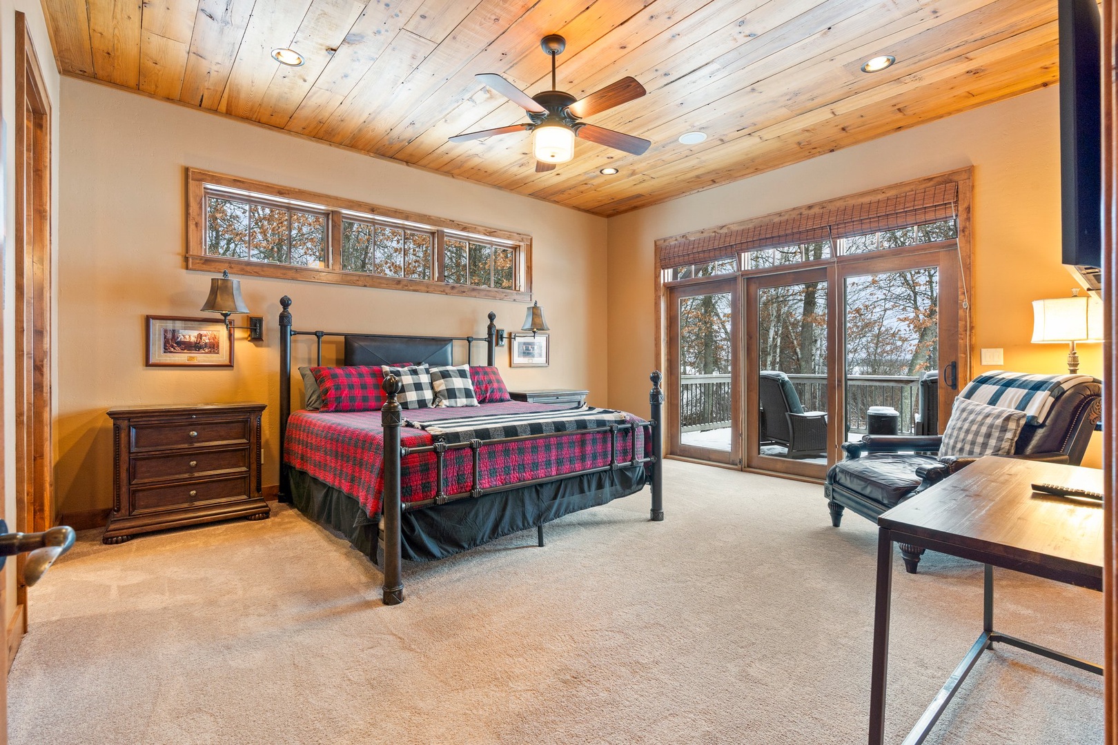 Primary Bedroom sanctuary features rustic wood ceilings, cozy plaid bedding, and large windows framing peaceful forest views from your private retreat.