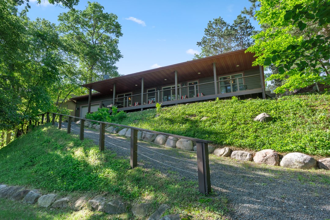 Modern cabin nestled on a tree-covered hillside, featuring a spacious deck and natural landscaping surrounded by lush greenery.