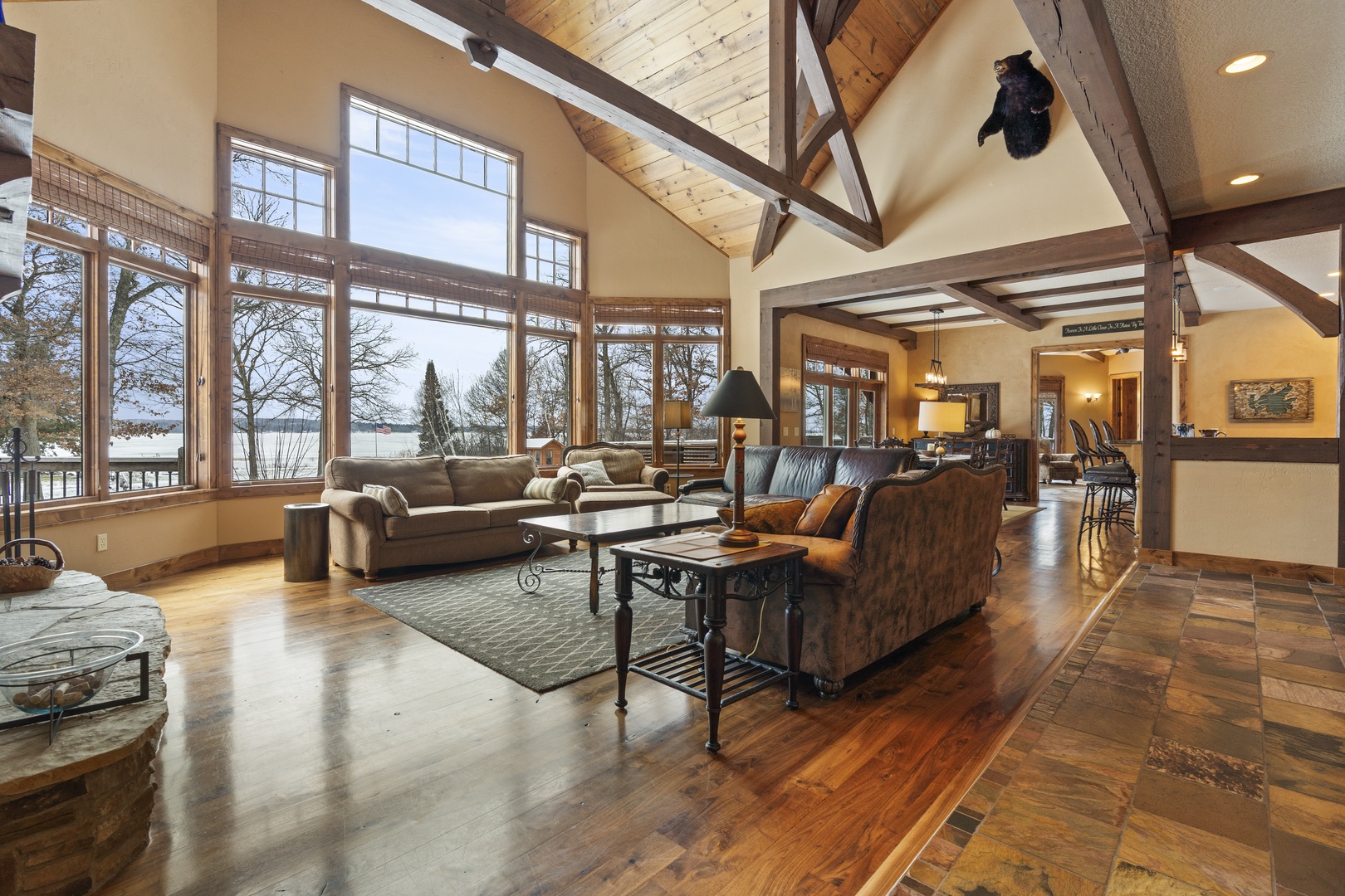 Unwind in this stunning great room where soaring timber beams frame panoramic lake views through floor-to-ceiling windows.