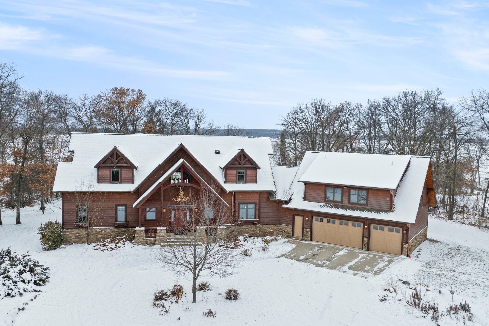 Snow-covered lodge featuring warm wood siding and mountain architecture, surrounded by mature trees in a peaceful winter setting.