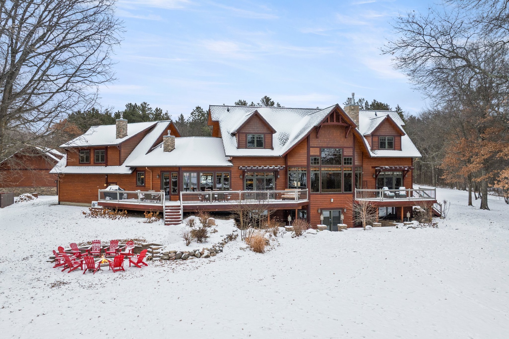 Beautiful lakefront lodge nestled in pristine winter wonderland, featuring rustic charm and multiple outdoor decks surrounded by snow-covered natural landscape.
