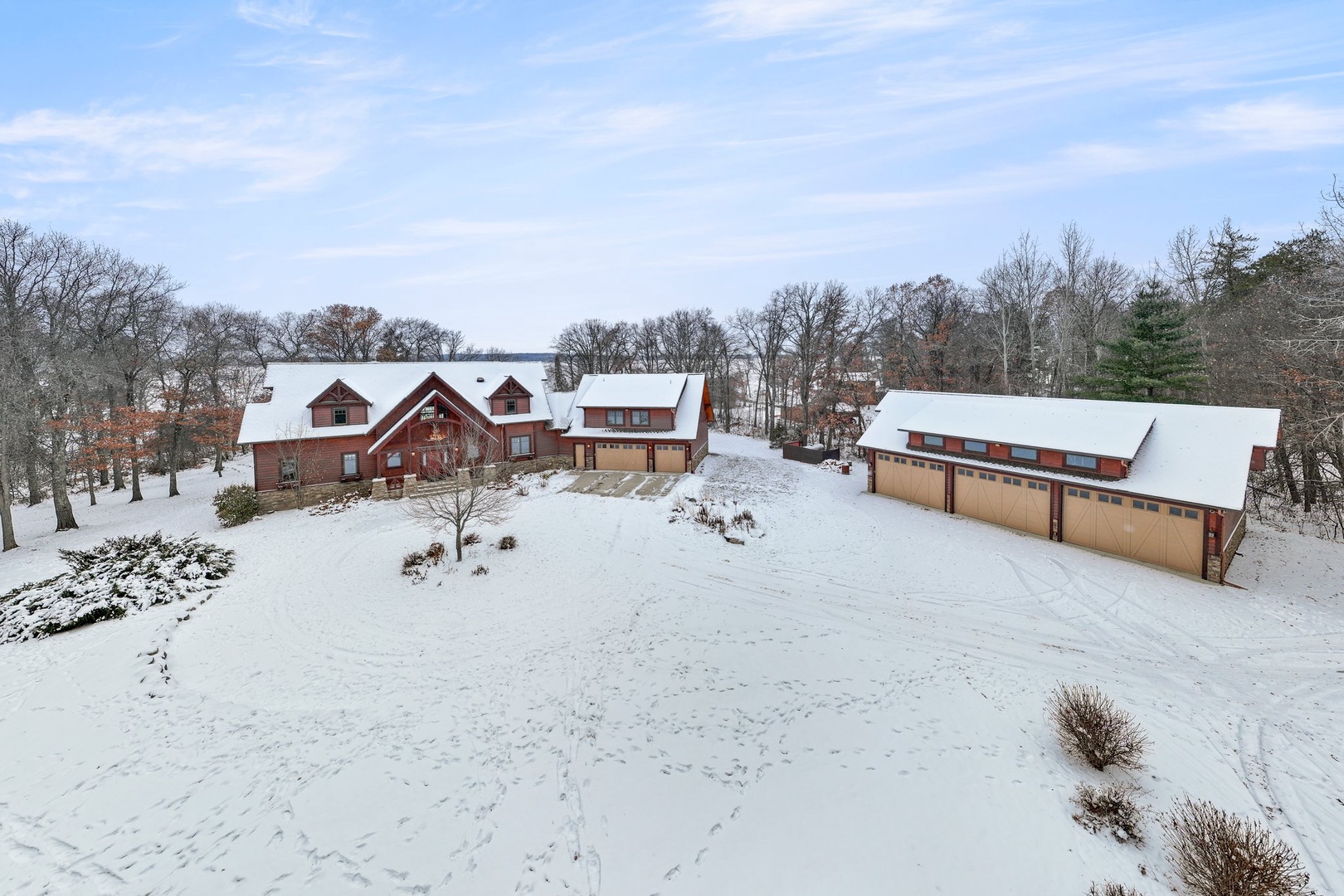 Beautiful property nestled among snow-covered grounds with spacious main building and separate garage structure surrounded by mature trees.