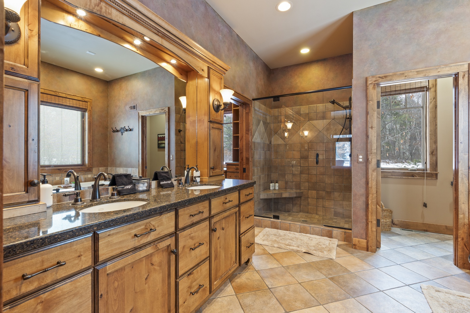 Indulge in your spacious master bathroom featuring dual vanities, a luxurious tiled shower, and elegant wood cabinetry for the ultimate relaxation.