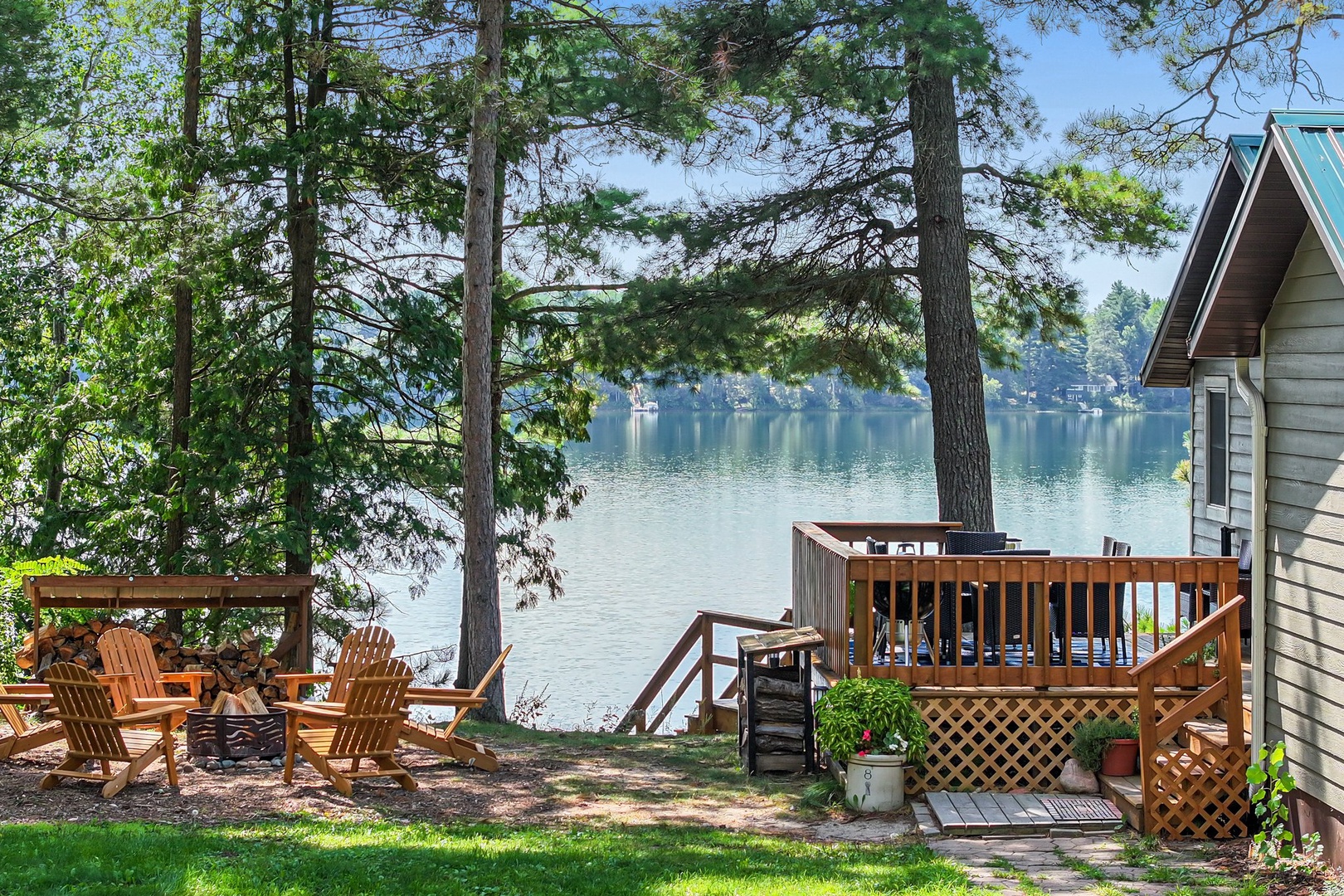 Lakefront cabin with wooden deck and Adirondack chairs surrounded by towering trees.