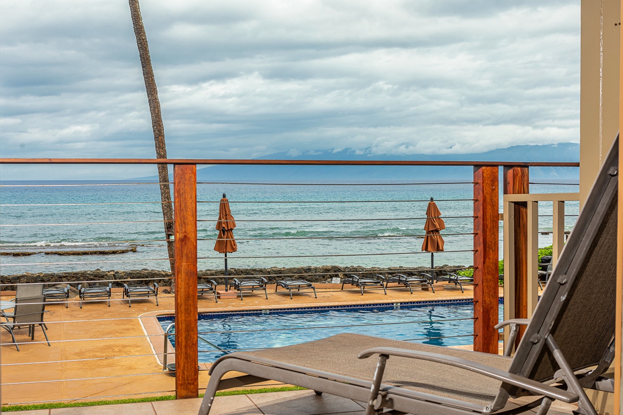 Oceanfront pool deck with lounge chairs, umbrellas, and stunning sea views framed by distant mountains—a perfect spot to unwind under open skies.