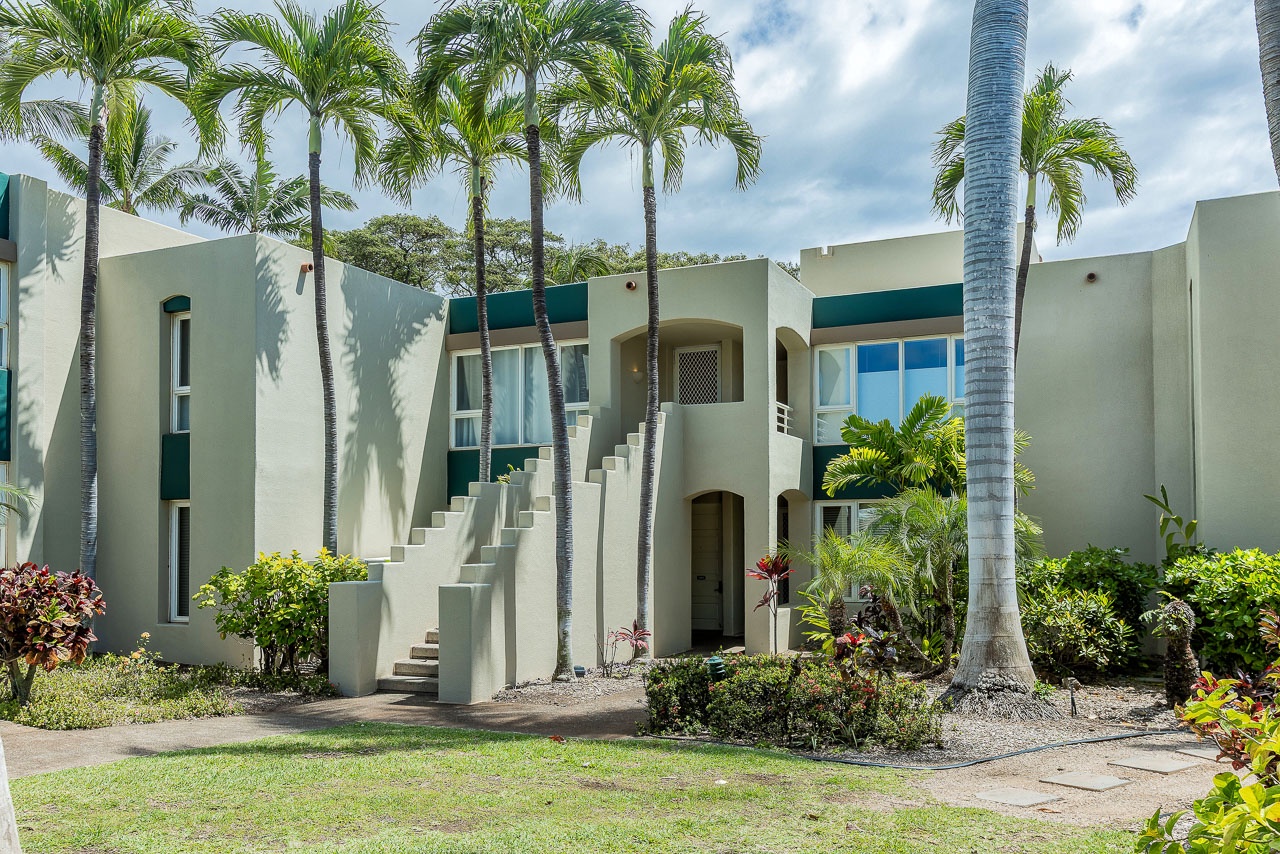 A tropical vacation rental property features contemporary architecture with palm trees, lush landscaping, and an exterior stairway leading to upper-level accommodations.