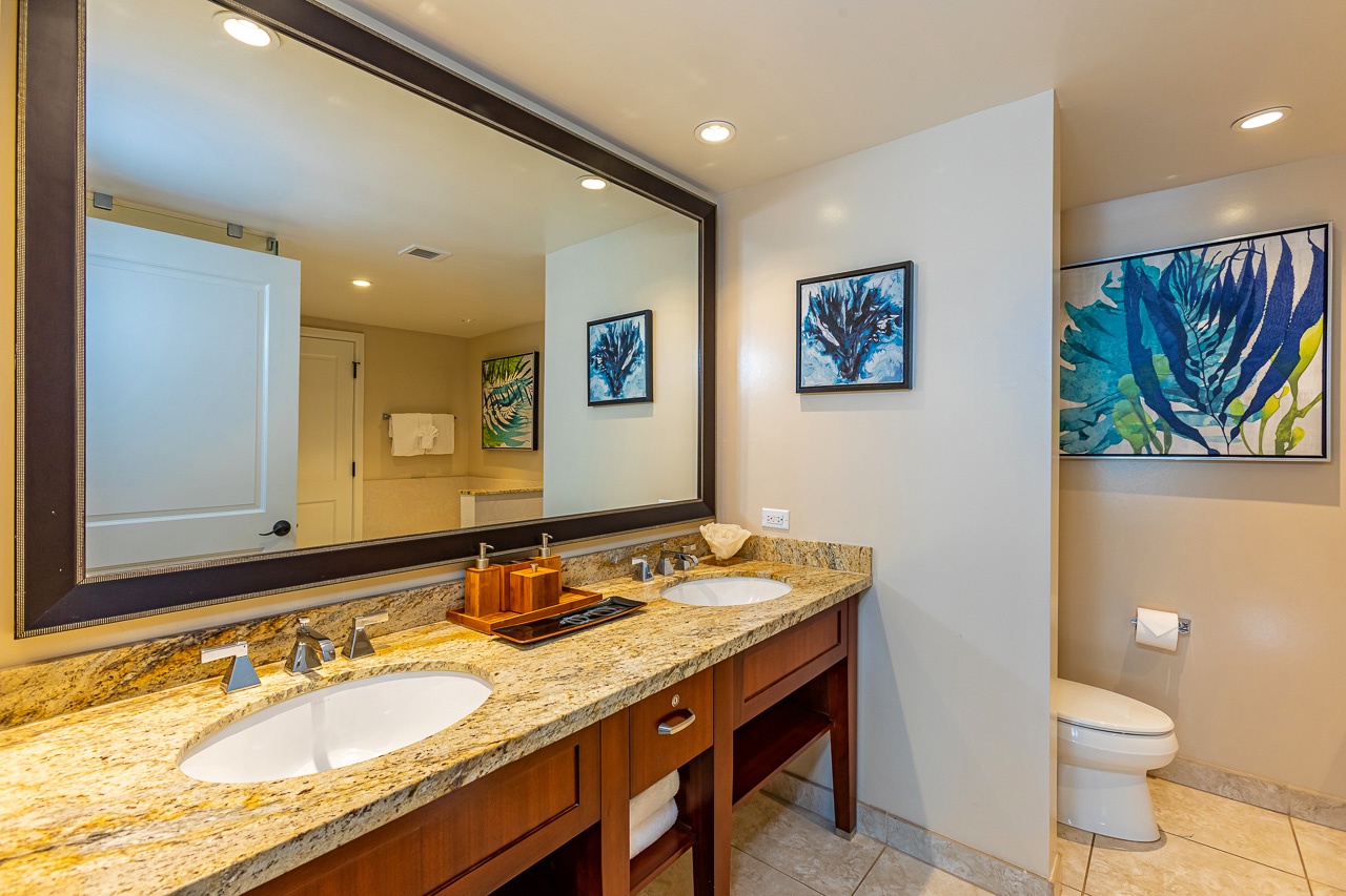 Spacious dual-sink vanity with rich wood cabinetry and granite countertops creates your own serene retreat. Vibrant coastal artwork adds a splash of island charm.