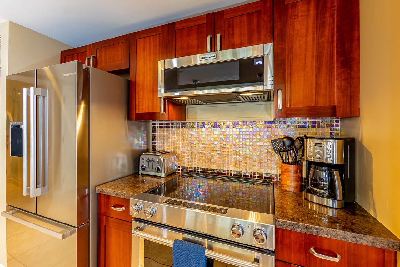 Your fully equipped kitchen features rich wood cabinetry, modern stainless steel appliances, and a vibrant tile backsplash that catches the light beautifully—perfect for preparing your favorite meals.