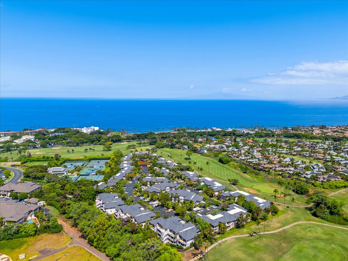 Aerial view of a coastal property nestled between a lush golf course and the sparkling blue Pacific Ocean, offering a serene Hawaiian escape.