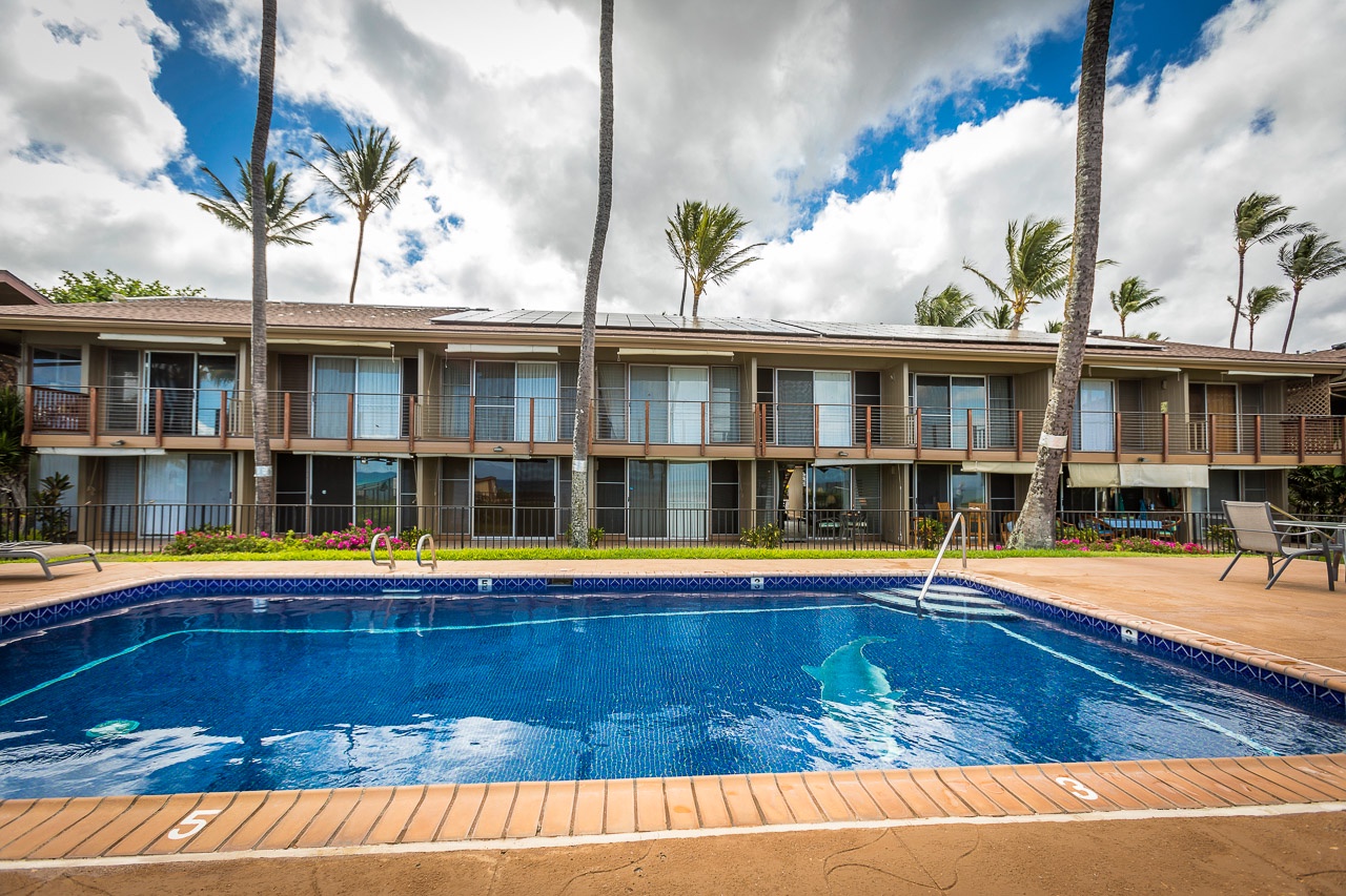 This tropical property features a sparkling pool framed by towering palm trees, with modern two-story accommodations offering private balconies overlooking the inviting outdoor space.