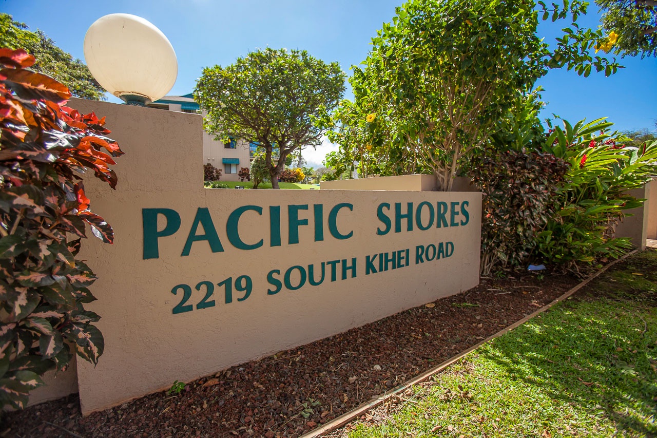 Pacific Shores property entrance sign surrounded by lush tropical landscaping and mature trees.