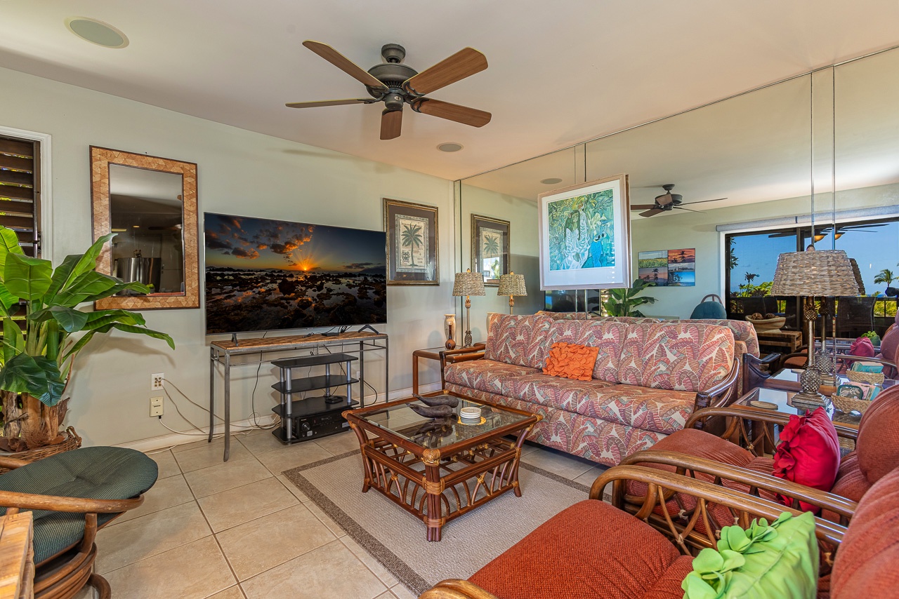 Relax in your bright, breezy living room with tropical touches, comfy seating, and stunning island sunsets on screen. Large windows frame lush views, inviting calm coastal vibes.