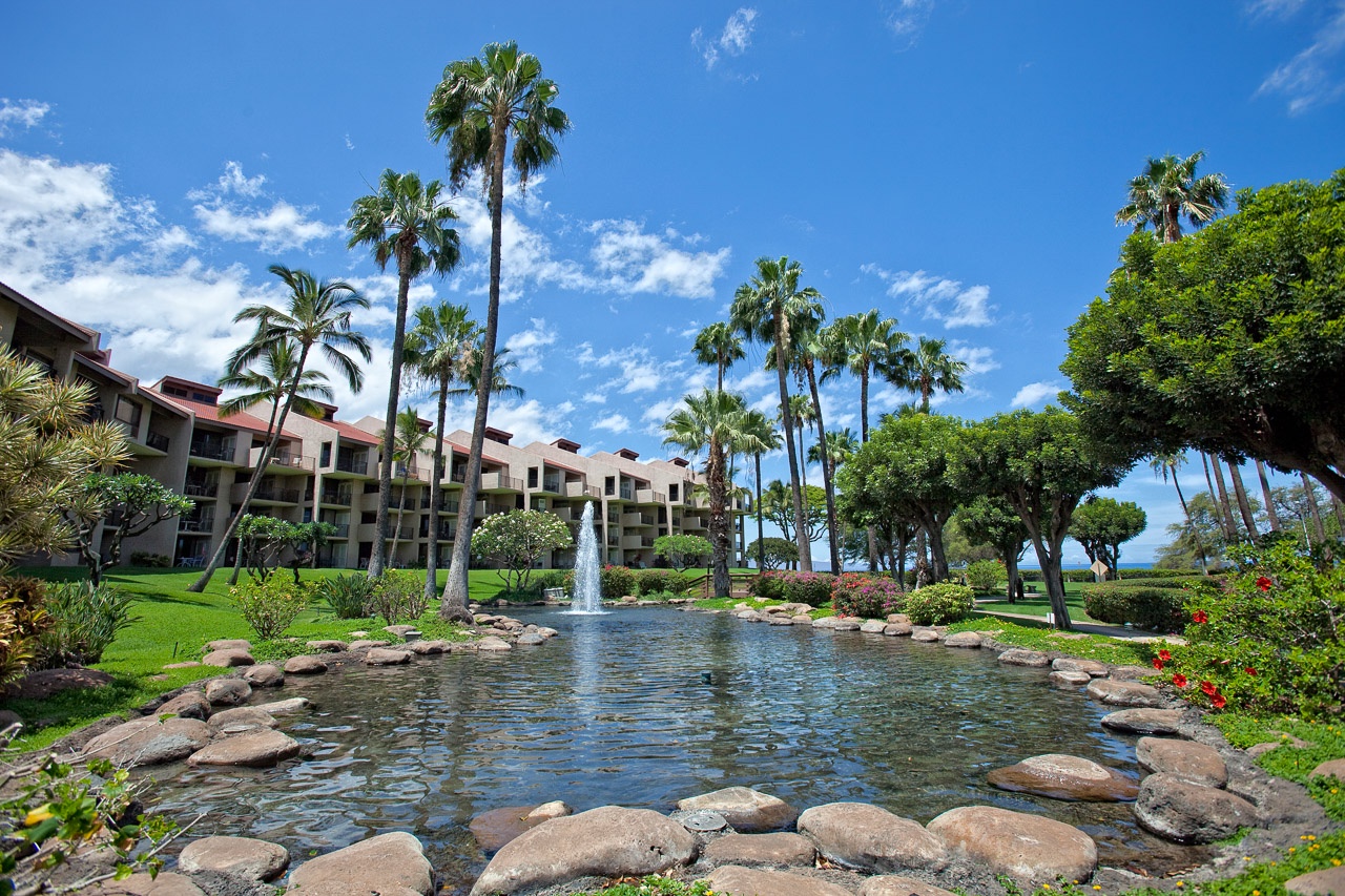Serene grounds featuring lush tropical gardens, swaying palm trees, and a peaceful fountain-fed pond surrounded by carefully landscaped greenery and seasonal blooms.