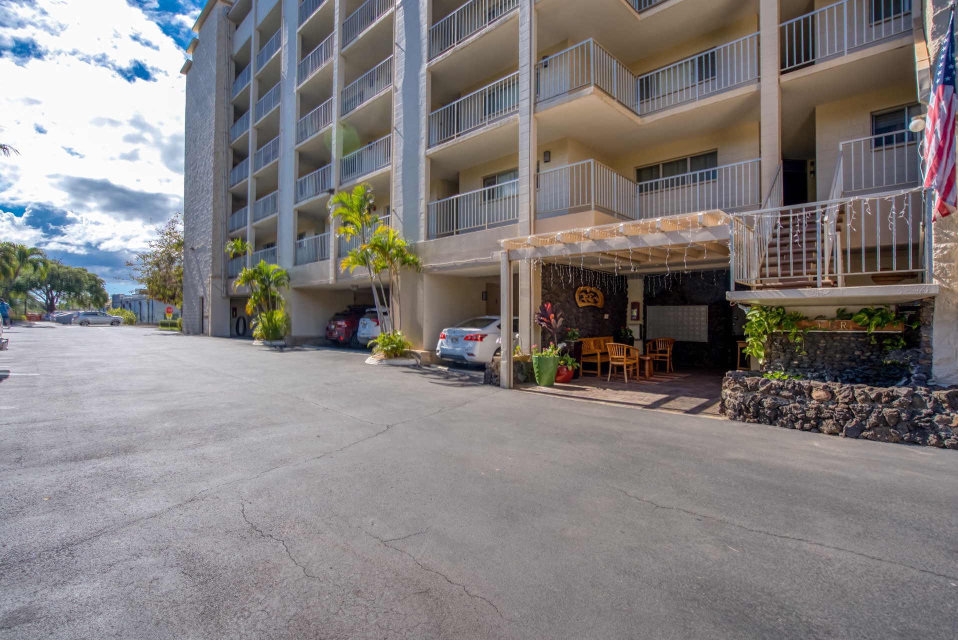 Beachfront building entrance with covered parking, tropical landscaping, balconies facing the waterfront, and convenient ground-level access to surrounding area amenities.