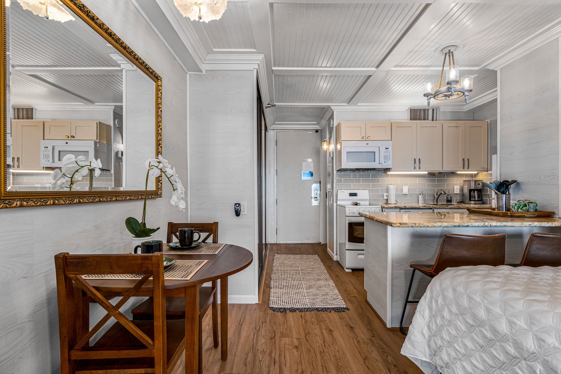 Step into your charming studio where the kitchenette, cozy dining nook, and plush bed blend seamlessly under elegant white-paneled ceilings—everything you need for a relaxed, restful stay.