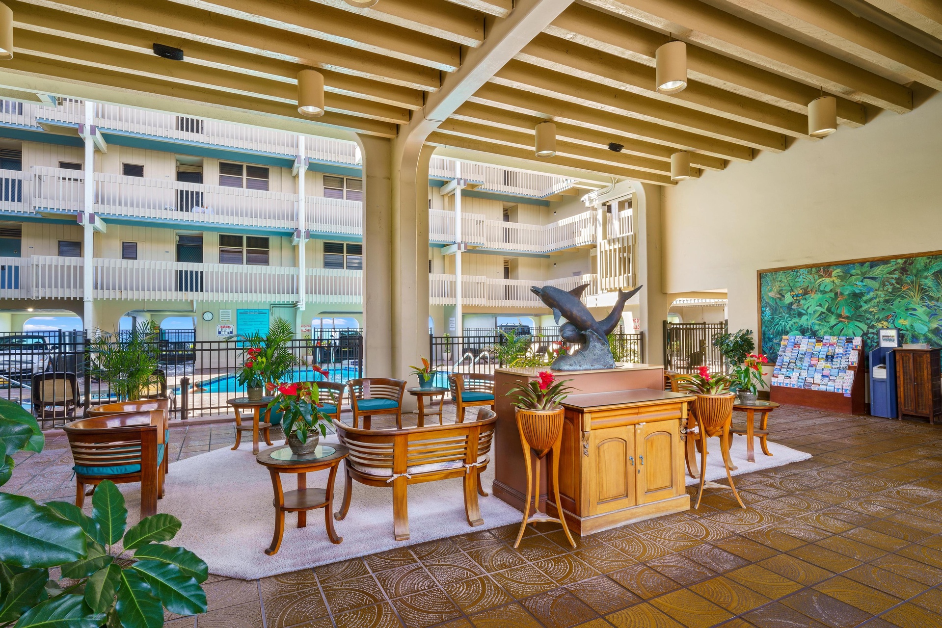 This welcoming lobby features tropical decor, comfortable seating, and a striking dolphin sculpture. Beyond the elegant wooden beams, you'll spot the inviting pool area framed by the property's balconies.
