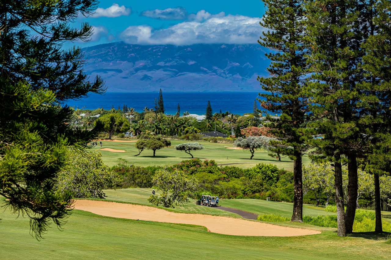 A stunning golf course framed by lush tropical landscaping, with sweeping mountain and ocean views defining the horizon.