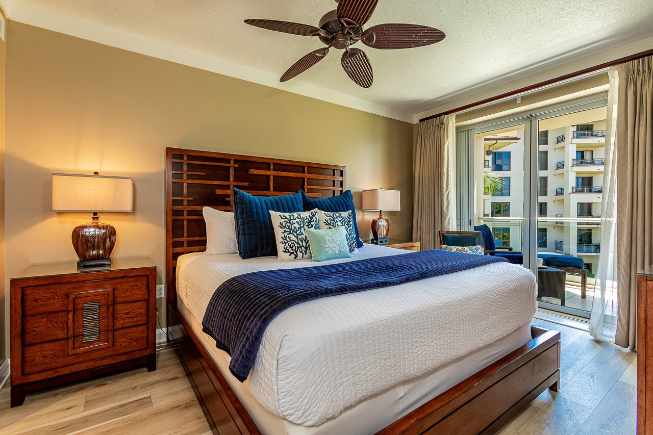 Sink into crisp linens in the primary bedroom from your private balcony—your peaceful retreat with ceiling fan comfort and warm island-inspired style awaits.