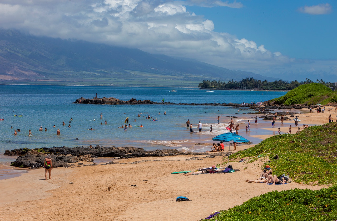 Golden sand, turquoise waters, and dramatic mountain backdrop define this stunning Hawaiian beach setting. Gentle waves and calm lagoon waters create an ideal spot for swimming and seaside relaxation.