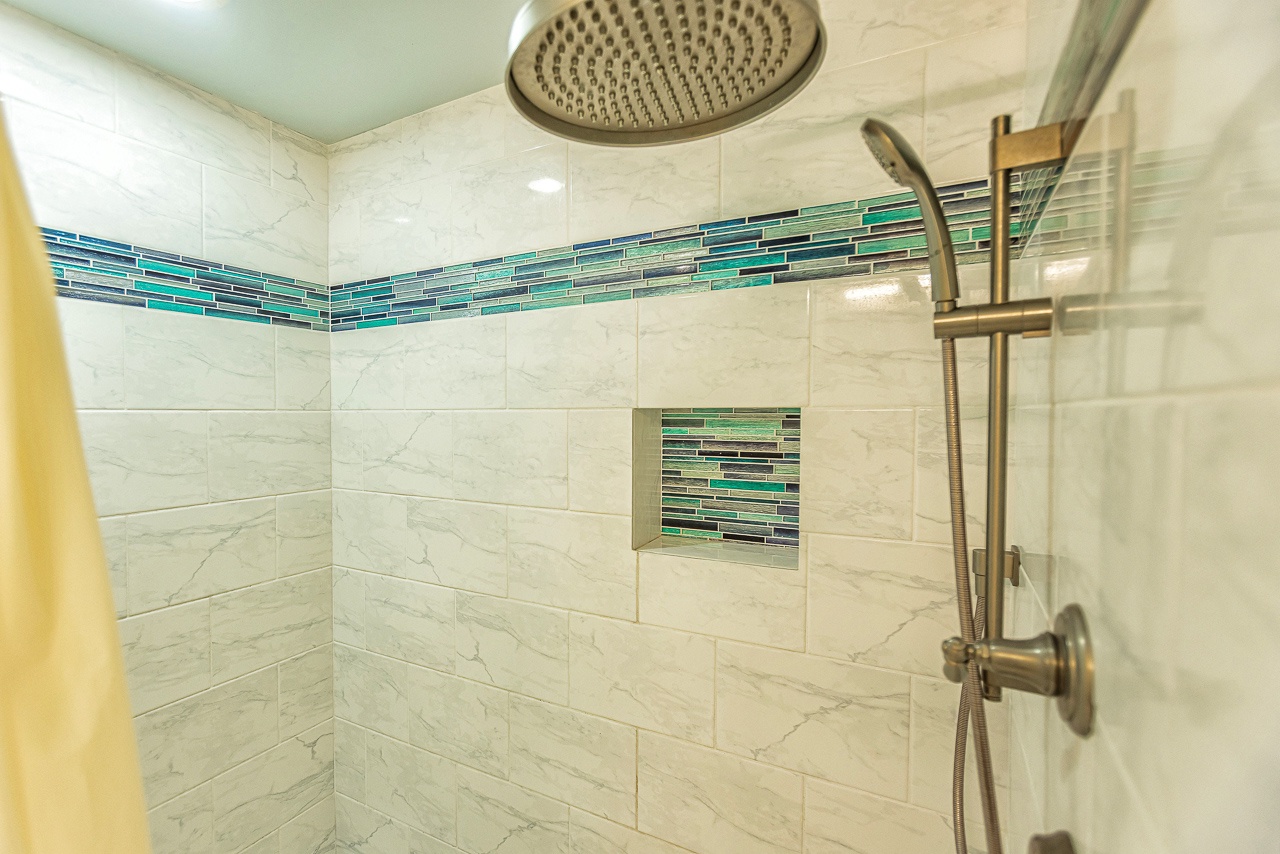 Step into your beautifully tiled shower featuring a rainfall head and handheld wand, with elegant turquoise accent tiles that add a spa-like touch to your daily routine.