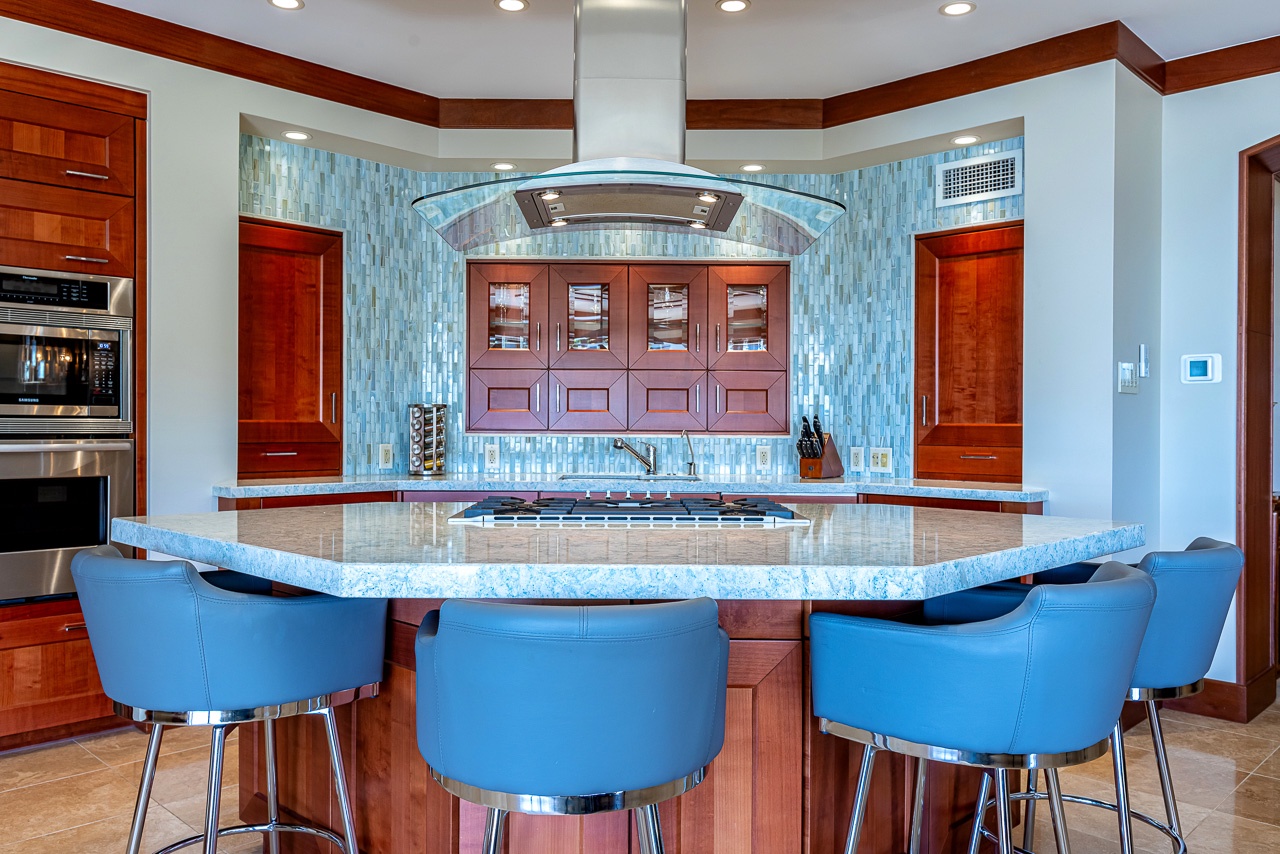 Gather around this stunning island where cooking becomes an experience. With a built-in cooktop at center stage and gleaming marble countertops, you'll craft your vacation meals in style beneath the elegant glass-canopy vent hood.