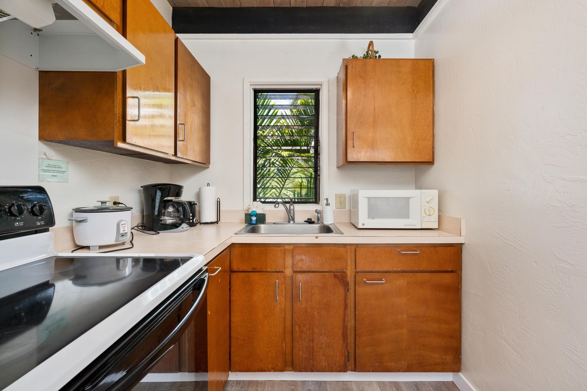 Your fully equipped kitchen features warm wood cabinetry, stainless steel appliances, and a garden window that fills the space with natural light and tropical views.