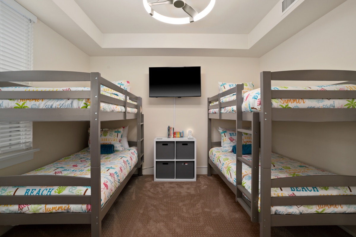Fun bunk room with colorful beach-themed bedding, wall-mounted TV for movie nights, and storage cubbies.