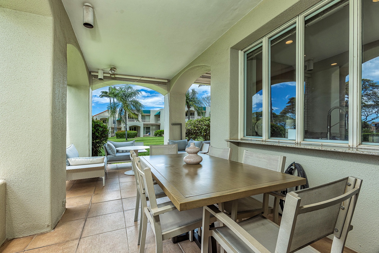 Your covered lanai welcomes you with a spacious dining table and cozy lounge seating, framed by elegant arches that open to lush tropical views and blue skies.
